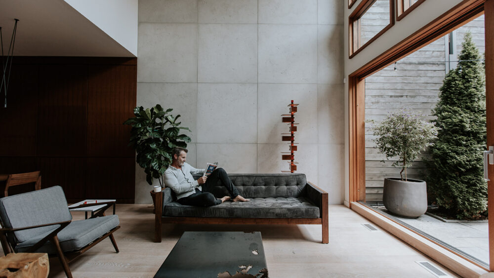 Stylish, modern living space designed with concrete cladding. Middle-aged man on a couch reading.