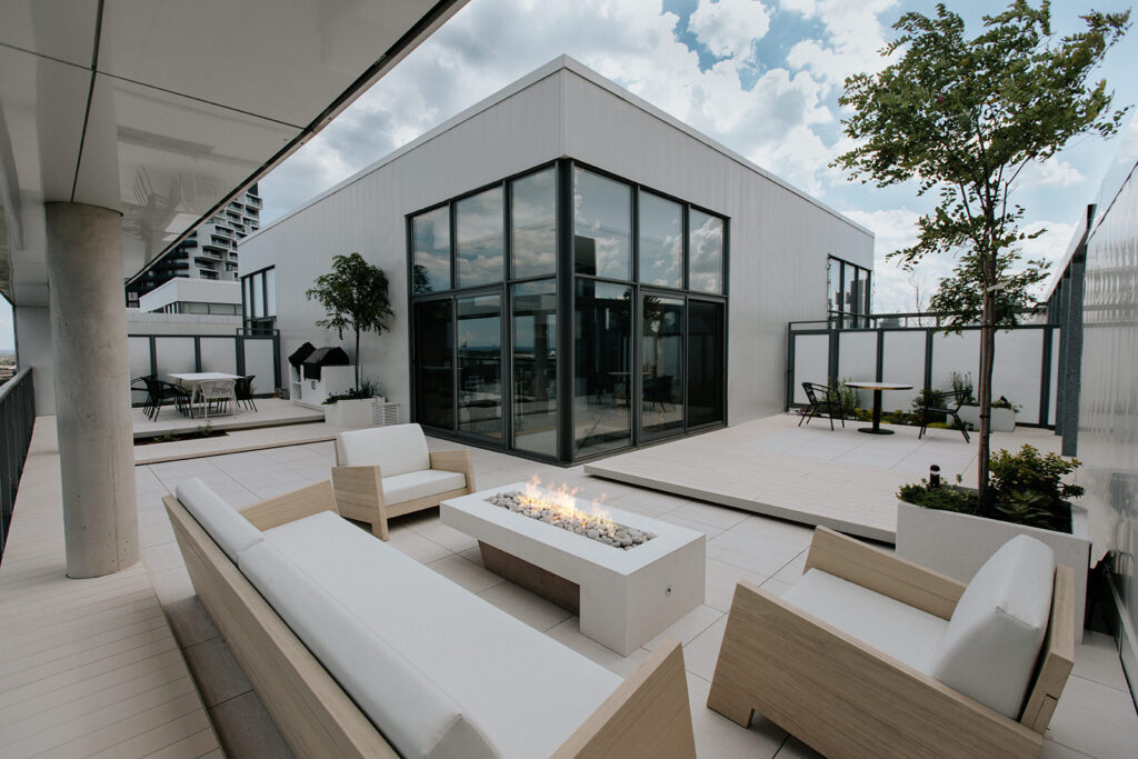 Outdoor patio with modern home in the distance. Patio features sitting areas, garden furniture and custom concrete fire pit. 