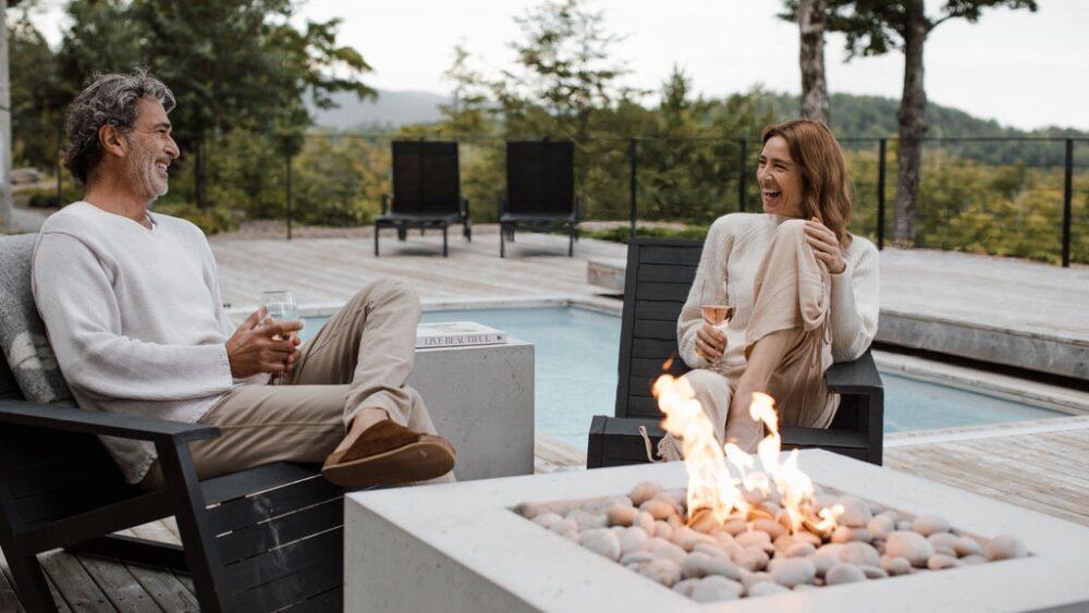 Man and woman sit next to a Dekko concrete fire pit on a hardwood deck.