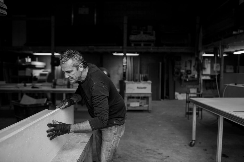 Older man working in a warehouse, sanding concrete panel. 